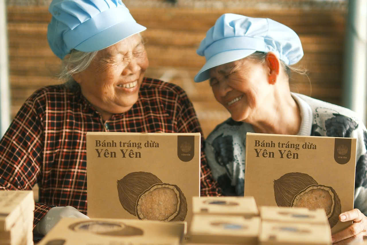 Hai cô tại xưởng Yên Yên cười vui bên những hộp bánh tráng dừa
